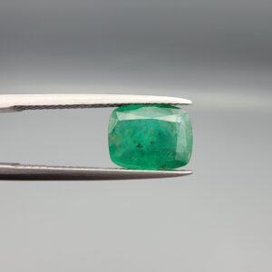 ​A premium 2.54-carat natural Pakistani Emerald gemstone resting flat on a white textured leather insert inside a display box. The loose, earth-mined beryl gem is precision cut into an elegant, well-proportioned cushion shape, exhibiting an incredibly rich, deep grass-green color with a classic velvety internal glow.
