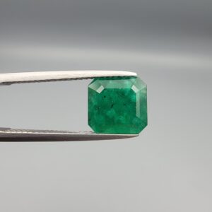 A premium 4.17-carat natural Swat Valley Emerald gemstone held securely in metal gemstone tweezers against a smooth gray studio background. The loose, earth-mined beryl gem is precision cut into an elegant octagon step-cut shape, showcasing an intense, saturated alpine-green color with fine symmetry and classic internal growth features.