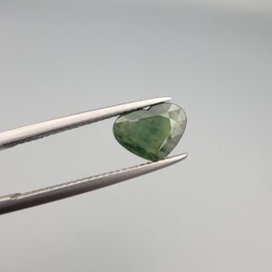 A rare 1.97-carat natural Green Sapphire gemstone held horizontally in professional steel gemstone tweezers against a smooth, neutral gray studio background. The loose Madagascar corundum crystal is masterfully faceted into a romantic heart shape, exhibiting a deeply saturated, sophisticated forest-green body color with fine facet symmetry and crisp meeting lines.