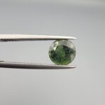 a premium, beautifully faceted 2.32-carat natural Green Sapphire gemstone is held securely in metal tweezers against a clean, neutral grey background. The loose corundum gem showcases an expert round cut with a well-proportioned table, displaying a rich, uniform olive-green color with fine, genuine internal crystal characteristics that verify its earth-mined origin.