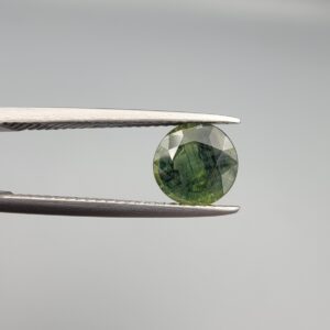 a premium, beautifully faceted 2.32-carat natural Green Sapphire gemstone is held securely in metal tweezers against a clean, neutral grey background. The loose corundum gem showcases an expert round cut with a well-proportioned table, displaying a rich, uniform olive-green color with fine, genuine internal crystal characteristics that verify its earth-mined origin.