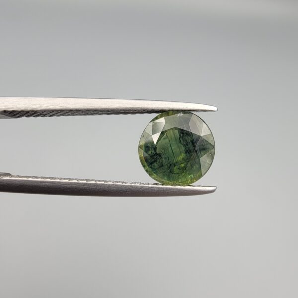 a premium, beautifully faceted 2.32-carat natural Green Sapphire gemstone is held securely in metal tweezers against a clean, neutral grey background. The loose corundum gem showcases an expert round cut with a well-proportioned table, displaying a rich, uniform olive-green color with fine, genuine internal crystal characteristics that verify its earth-mined origin.