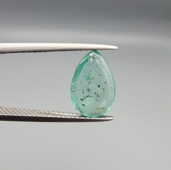 ​A 2.06-carat natural Colombian Emerald gemstone held vertically in professional metal gemstone tweezers against a smooth gray studio background. The loose gem is fashioned into a graceful pear shape, displaying a highly authentic, transparent mint-to-forest green core filled with dense, raw internal mountain fissures, natural inclusions, and soft organic mineral cracks.