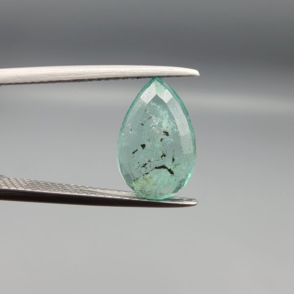 ​A 2.06-carat natural Colombian Emerald gemstone held vertically in professional metal gemstone tweezers against a smooth gray studio background. The loose gem is fashioned into a graceful pear shape, displaying a highly authentic, transparent mint-to-forest green core filled with dense, raw internal mountain fissures, natural inclusions, and soft organic mineral cracks.