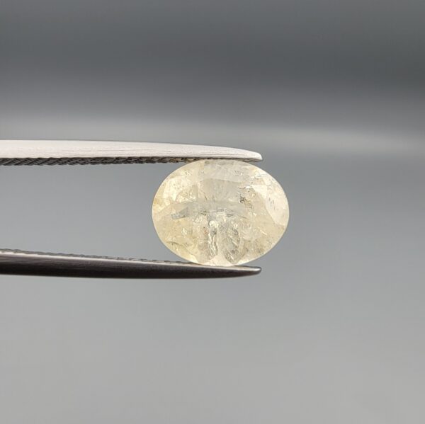 A premium, high-clarity 2.67-carat natural Ceylon Yellow Sapphire gemstone held horizontally in professional steel gemstone tweezers against a smooth gray studio background. The loose Sri Lankan Pukhraj features an elegant faceted oval cut, displaying a vibrant, evenly distributed lemon-yellow color profile with immaculate crown facet symmetry and intense internal light refraction.