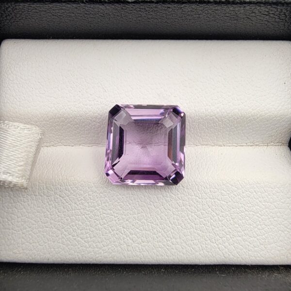 A high-clarity 6.38-carat natural Brazilian Amethyst gemstone nestled securely in a luxury white-cushioned black leather display box. The loose gem showcases a crisp octagon step cut, displaying an exceptionally even light-to-medium purple color profile with immaculate parallel symmetry and an eye-clean, mirror-polished table.