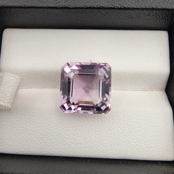 A prominent, high-clarity 10.22-carat natural Brazilian Amethyst gemstone showcased inside a white-cushioned black leatherette display box. The loose gem displays a precision octagon step cut with sharp parallel outlines, emphasizing an intensely rich, uniform deep violet color profile with an immaculate mirror-polished table.
