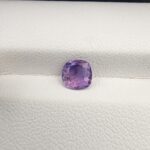 ​A premium, high-clarity 1.22-carat natural Ceylon Purple Sapphire gemstone nestled securely in a luxury white-cushioned black display box. The loose gem showcases an elegant faceted cushion cut with beautifully soft edges, displaying an intensely saturated, deep royal purple and vibrant violet body color with pristine facet symmetry and outstanding internal light reflection.