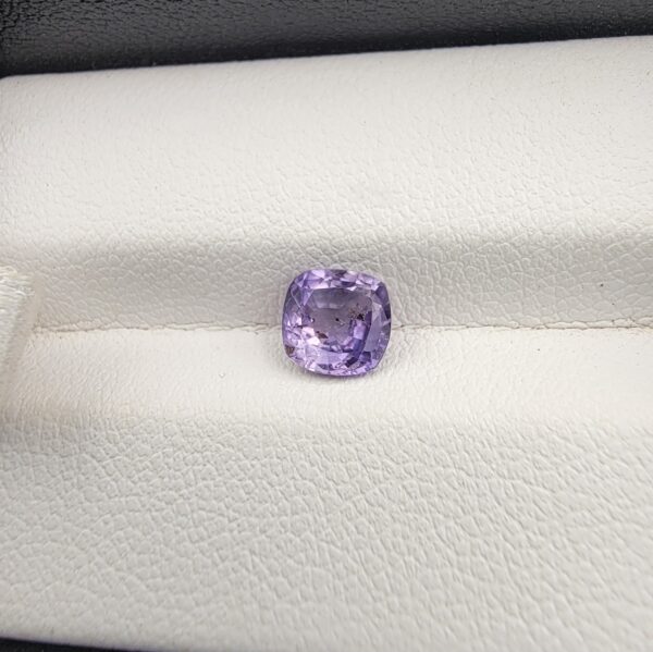 ​A premium, high-clarity 1.21-carat natural Ceylon Purple Sapphire gemstone nestled securely in a luxury white-cushioned black display box. The loose gem showcases an elegant faceted cushion cut with beautifully soft edges, displaying an intensely saturated, deep royal purple and vibrant violet body color with pristine facet symmetry and outstanding internal light reflection.