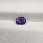 A rare, high-clarity 0.67-carat natural Ceylon Purple Sapphire gemstone nestled securely in a luxury white-cushioned black display box. The loose gem showcases an elegant faceted oval cut, displaying an intensely saturated deep violet-purple to royal purple body color with outstanding internal light refraction and pristine facet symmetry.