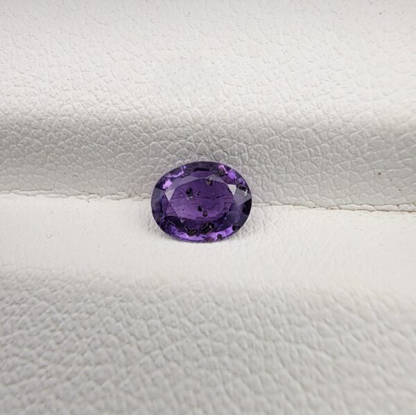 A rare, high-clarity 0.67-carat natural Ceylon Purple Sapphire gemstone nestled securely in a luxury white-cushioned black display box. The loose gem showcases an elegant faceted oval cut, displaying an intensely saturated deep violet-purple to royal purple body color with outstanding internal light refraction and pristine facet symmetry.