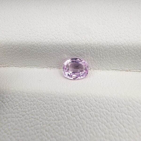 A premium, high-clarity 0.58-carat natural Ceylon Light Purple Sapphire gemstone nestled securely in a luxury white-cushioned display box. The loose gem showcases an elegant faceted cushion cut, displaying a delicate, brightly saturated light violet-purple body color with excellent internal light refraction and pristine facet symmetry.