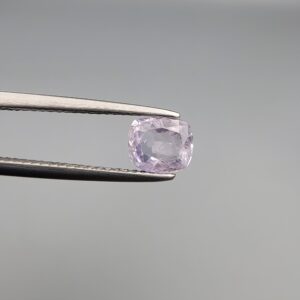 A premium, high-clarity 1.08-carat natural Ceylon Light Purple Sapphire gemstone held securely in metal tweezers against a clean grey background. The loose gem showcases an elegant faceted cushion cut with beautifully balanced crown facets, displaying a delicate, brightly translucent light violet-purple body color with excellent internal light reflection and pristine facet symmetry.