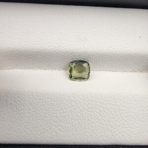 A rare, high-clarity 0.63-carat natural Ceylon Green Sapphire gemstone nestled securely in a luxury white-cushioned display box. The loose gem showcases an elegant faceted cushion cut, displaying a delicate, brightly saturated pastel mint green body color with outstanding internal light refraction and pristine facet symmetry.