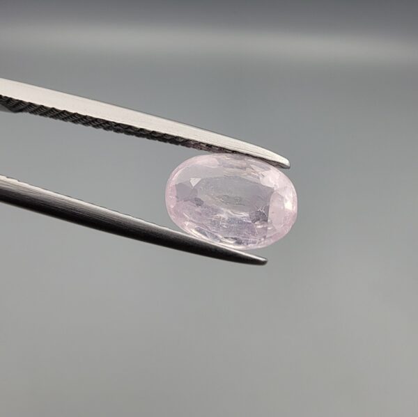 A premium, high-clarity 1.78-carat natural Ceylon Light Pink Sapphire gemstone held securely in metal tweezers against a clean grey background. The loose gem showcases an elegant faceted oval cut with beautifully balanced proportions, displaying a delicate, brightly translucent pastel pink body color with pristine facet symmetry, zero enhancements, and exceptional internal light reflection.