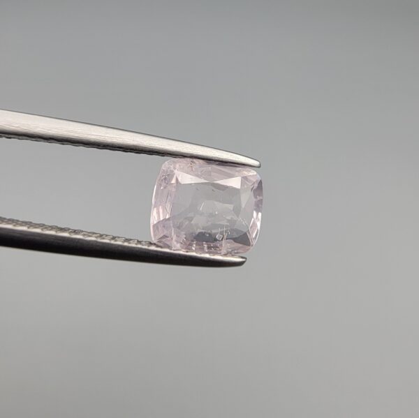 ​A premium, high-clarity 1.50-carat natural Ceylon Light Pink Sapphire gemstone held securely in metal tweezers against a clean, neutral grey background. The loose gem showcases an elegant faceted cushion cut with beautifully sharp facet junctions, displaying a delicate, softly translucent pastel pink body color with pristine facet symmetry, zero enhancements, and exceptional internal light refraction.