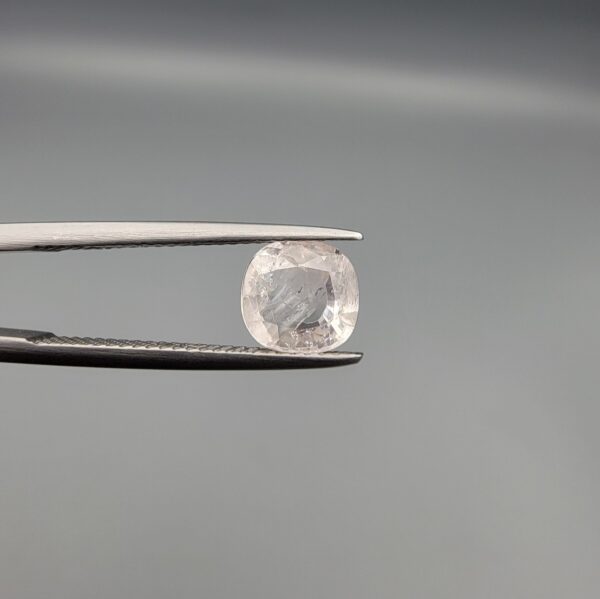 ​A rare, high-clarity 1.64-carat natural Ceylon Light Peach Sapphire gemstone held securely in metal tweezers against a clean, professional grey background. The loose gem showcases a premium faceted cushion cut with beautifully soft corners, displaying an intensely bright, pastel peach-champagne body color with exquisite facet symmetry, zero enhancements, and superb internal light reflection.