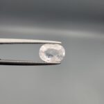 a premium, high-translucency 1.94-carat natural Ceylon White Sapphire gemstone is held securely in metal tweezers against a clean, neutral grey background. The loose gemstone showcases an expert faceted oval cut, displaying a completely colorless body with exceptional internal light reflection, icy diamond-like brilliance, and fine natural internal crystal characteristics that verify its completely untreated origin.