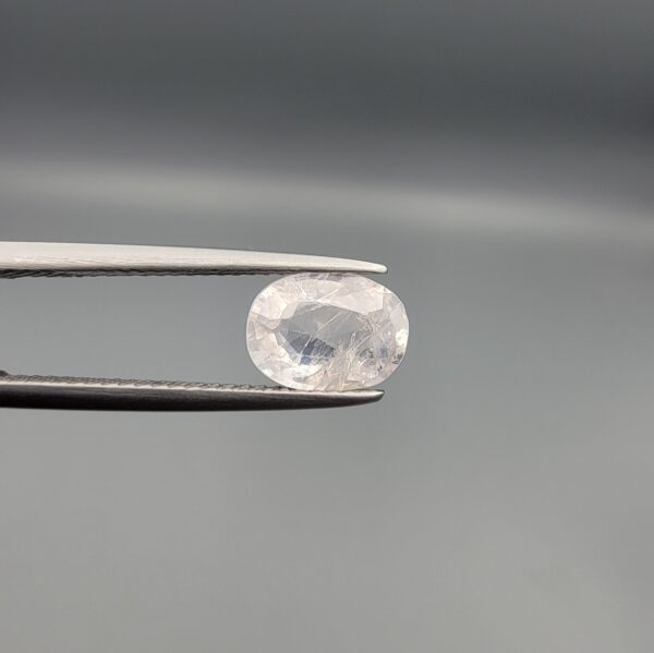 a premium, high-translucency 1.94-carat natural Ceylon White Sapphire gemstone is held securely in metal tweezers against a clean, neutral grey background. The loose gemstone showcases an expert faceted oval cut, displaying a completely colorless body with exceptional internal light reflection, icy diamond-like brilliance, and fine natural internal crystal characteristics that verify its completely untreated origin.