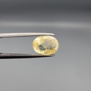 a premium, beautifully faceted 3.22-carat natural Yellow Sapphire gemstone is held securely in metal tweezers against a clean, neutral grey background. The loose corundum gem showcases an expert oval cut with a well-proportioned table, displaying a bright, light-yellow color with fine, genuine internal crystal characteristics and natural feather inclusions that verify its rare, unheated earth-mined origin.