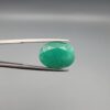 a premium, beautifully faceted 8.50-carat natural Emerald gemstone is held securely in metal tweezers against a clean, neutral grey background. The loose beryl gem showcases an expert oval cut with a well-proportioned table, displaying a rich, uniform green color with fine, genuine internal crystal characteristics and natural inclusions that verify its authentic earth-mined origin.