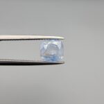 a premium, beautifully faceted 2.95-carat natural Blue Sapphire gemstone is held securely in metal tweezers against a clean, neutral grey background. The loose corundum gem showcases an expert cushion cut with a well-proportioned table, displaying an icy light-blue color with fine, genuine internal crystal characteristics and natural feather inclusions that verify its rare, unheated earth-mined origin.