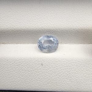 a premium, beautifully faceted 1.76-carat natural Blue Sapphire gemstone rests inside a white leatherette display box. The loose corundum gem showcases an expert oval cut with a well-proportioned table, displaying a serene, icy light-blue tone with fine, genuine internal crystal characteristics that verify its rare, unheated earth-mined origin
