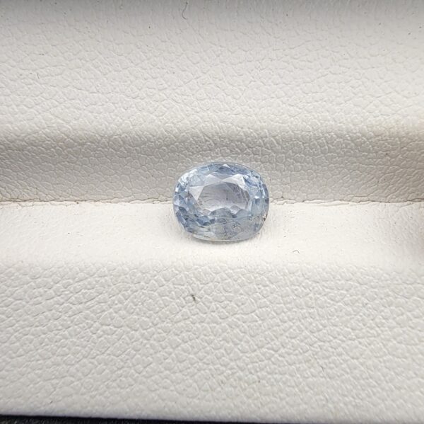 a premium, beautifully faceted 1.76-carat natural Blue Sapphire gemstone rests inside a white leatherette display box. The loose corundum gem showcases an expert oval cut with a well-proportioned table, displaying a serene, icy light-blue tone with fine, genuine internal crystal characteristics that verify its rare, unheated earth-mined origin