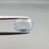 a premium, beautifully faceted 1.37-carat natural Blue Sapphire gemstone is held securely in metal tweezers against a clean, neutral grey background. The loose cushion-cut corundum gem displays a delicate icy light-blue hue with distinctive, beautiful internal silk and crystal inclusions that serve as a natural fingerprint, verifying its unheated earth-mined origin.