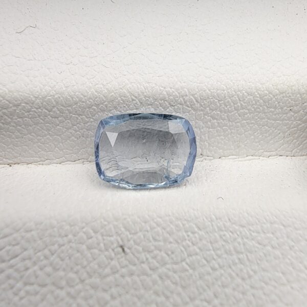 a premium, beautifully faceted 1.37-carat natural Blue Sapphire gemstone is held securely in metal tweezers against a clean, neutral grey background. The loose cushion-cut corundum gem displays a delicate icy light-blue hue with distinctive, beautiful internal silk and crystal inclusions that serve as a natural fingerprint, verifying its unheated earth-mined origin.