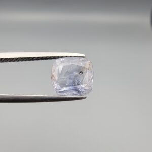 a premium, beautifully faceted 3.62-carat natural Blue Sapphire gemstone is held securely in metal tweezers against a clean, neutral grey background. The loose cushion-cut corundum gem displays a delicate icy light-blue color with a prominent natural internal cavity and fine crystal inclusions that serve as an indisputable signature of its unheated, earth-mined origin.