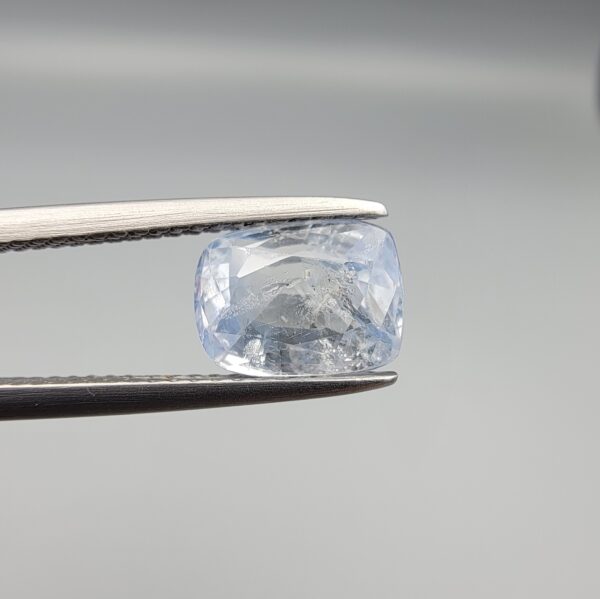 A premium, beautifully faceted 2.37-carat natural Blue Sapphire gemstone rests inside a white leatherette display box. The loose cushion-cut corundum gem displays a soft, icy light-blue tone with fine internal silk and genuine crystal characteristics that serve as an indisputable signature of its unheated, earth-mined origin.