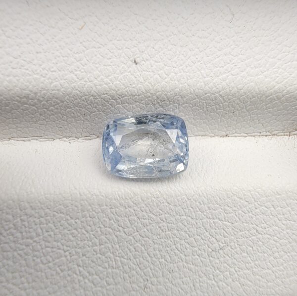 A premium, beautifully faceted 2.37-carat natural Blue Sapphire gemstone rests inside a white leatherette display box. The loose cushion-cut corundum gem displays a soft, icy light-blue tone with fine internal silk and genuine crystal characteristics that serve as an indisputable signature of its unheated, earth-mined origin.