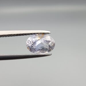 A premium, beautifully faceted 1.93-carat natural Blue Sapphire gemstone is held securely in metal tweezers against a clean, neutral grey background. The loose oval-cut corundum gem displays a soft icy light-blue tone with fine internal silk and distinct golden-yellow mineral inclusions that serve as an indisputable signature of its unheated, earth-mined origin.