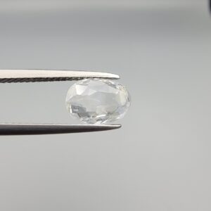 A premium, beautifully faceted 2.07-carat natural White Sapphire gemstone is held securely in metal tweezers against a clean, neutral grey background. The loose oval-cut corundum gem displays a completely colorless, diamond-like clarity with fine internal silk and natural crystal growth features that serve as an indisputable signature of its unheated, earth-mined origin.