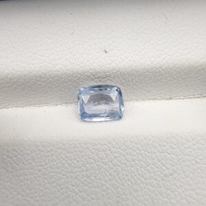 A premium, beautifully faceted 1.27-carat natural Blue Sapphire gemstone rests inside a white leatherette display box. The loose cushion-cut corundum gem displays a serene, icy light-blue tone with fine internal silk and natural micro-crystal inclusions that serve as an indisputable signature of its unheated, earth-mined origin.