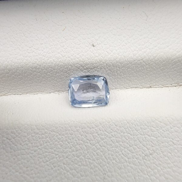 A premium, beautifully faceted 1.27-carat natural Blue Sapphire gemstone rests inside a white leatherette display box. The loose cushion-cut corundum gem displays a serene, icy light-blue tone with fine internal silk and natural micro-crystal inclusions that serve as an indisputable signature of its unheated, earth-mined origin.