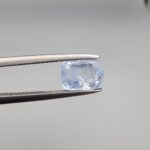 A premium, beautifully faceted 1.93-carat natural Blue Sapphire gemstone is held securely in metal tweezers against a clean, neutral grey background. The loose cushion-cut corundum gem displays a soft icy light-blue tone with fine internal silk and natural mineral inclusions that serve as an indisputable signature of its unheated, earth-mined origin.