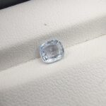 A premium, beautifully faceted 1.09-carat natural Blue Sapphire gemstone rests inside a white leatherette display box. The loose cushion-cut corundum gem displays a soft, icy light-blue tone with fine internal silk and genuine crystal growth characteristics that serve as an indisputable signature of its unheated, earth-mined origin.