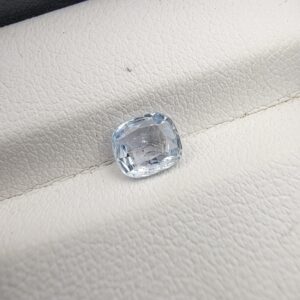 A premium, beautifully faceted 1.09-carat natural Blue Sapphire gemstone rests inside a white leatherette display box. The loose cushion-cut corundum gem displays a soft, icy light-blue tone with fine internal silk and genuine crystal growth characteristics that serve as an indisputable signature of its unheated, earth-mined origin.