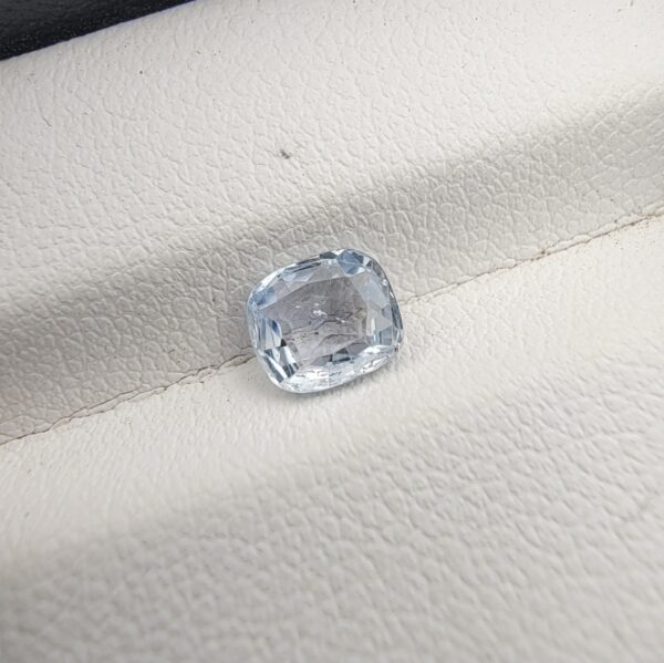 A premium, beautifully faceted 1.09-carat natural Blue Sapphire gemstone rests inside a white leatherette display box. The loose cushion-cut corundum gem displays a soft, icy light-blue tone with fine internal silk and genuine crystal growth characteristics that serve as an indisputable signature of its unheated, earth-mined origin.