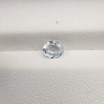 A premium, beautifully faceted 0.68-carat natural White Sapphire gemstone rests inside a white leatherette display box. The loose oval-cut corundum gem displays a completely colorless, diamond-like clarity with fine internal silk and natural crystal growth features that serve as an indisputable signature of its unheated, earth-mined origin.