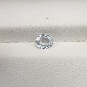 A premium, beautifully faceted 0.68-carat natural White Sapphire gemstone rests inside a white leatherette display box. The loose oval-cut corundum gem displays a completely colorless, diamond-like clarity with fine internal silk and natural crystal growth features that serve as an indisputable signature of its unheated, earth-mined origin.