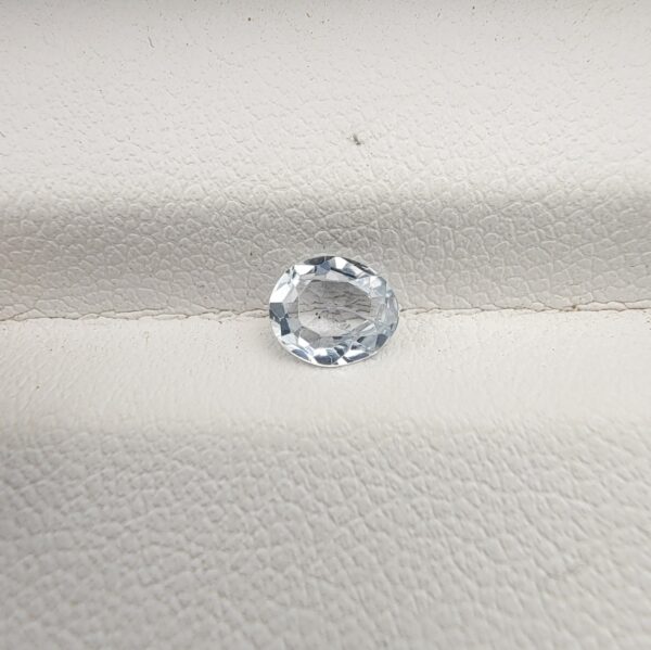 A premium, beautifully faceted 0.68-carat natural White Sapphire gemstone rests inside a white leatherette display box. The loose oval-cut corundum gem displays a completely colorless, diamond-like clarity with fine internal silk and natural crystal growth features that serve as an indisputable signature of its unheated, earth-mined origin.