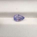 A premium, beautifully faceted 1.85-carat natural Purplish Blue Sapphire gemstone rests inside a white leatherette display box. The loose pear-cut corundum gem displays a unique violet-blue body tone with soft yellow mineral inclusions that serve as an indisputable signature of its unheated, earth-mined origin.