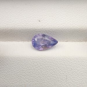 A premium, beautifully faceted 1.85-carat natural Purplish Blue Sapphire gemstone rests inside a white leatherette display box. The loose pear-cut corundum gem displays a unique violet-blue body tone with soft yellow mineral inclusions that serve as an indisputable signature of its unheated, earth-mined origin.