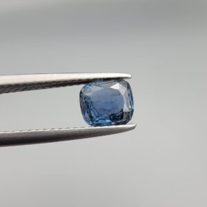 A premium, beautifully faceted 1.42-carat natural Deep Blue Sapphire gemstone is held securely in metal tweezers against a clean, neutral grey background. The loose cushion-cut corundum gem displays a rich, intense deep-blue hue with fine internal silk and genuine crystal growth characteristics that serve as an indisputable signature of its unheated, earth-mined origin.