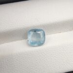 A premium, beautifully faceted 2.23-carat natural Ice Blue Sapphire gemstone rests inside a white leatherette display box. The loose cushion-cut corundum gem displays a serene, very light ice-blue tone with fine internal silk and natural mineral features that serve as an indisputable signature of its unheated, earth-mined origin.