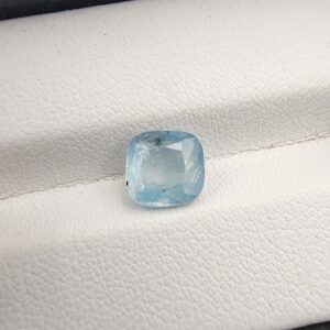 A premium, beautifully faceted 2.23-carat natural Ice Blue Sapphire gemstone rests inside a white leatherette display box. The loose cushion-cut corundum gem displays a serene, very light ice-blue tone with fine internal silk and natural mineral features that serve as an indisputable signature of its unheated, earth-mined origin.