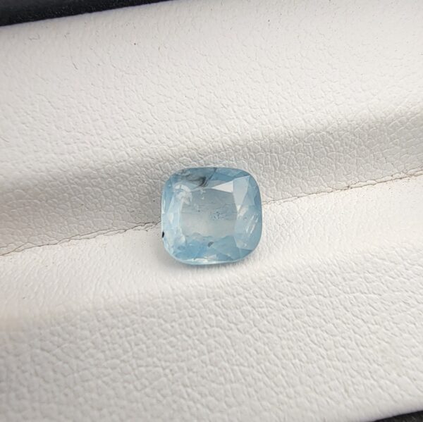 A premium, beautifully faceted 2.23-carat natural Ice Blue Sapphire gemstone rests inside a white leatherette display box. The loose cushion-cut corundum gem displays a serene, very light ice-blue tone with fine internal silk and natural mineral features that serve as an indisputable signature of its unheated, earth-mined origin.